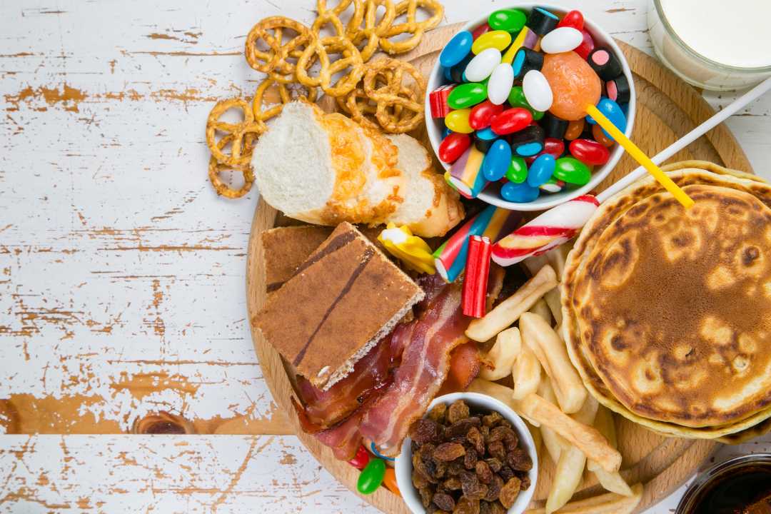 A variety of high-glycemic foods including candy, pancakes, white bread, and fries, illustrating foods to avoid for better glycemic control and sustained energy.