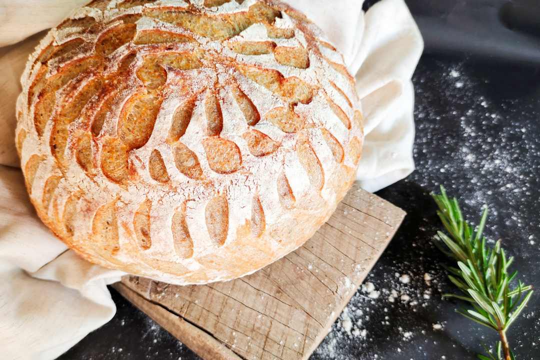 A beautifully scored loaf of sourdough bread on a wooden board, showcasing why sourdough is a healthier and more nutritious bread choice.