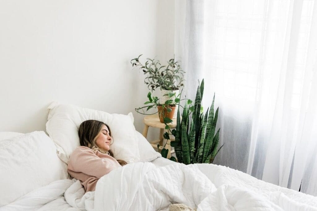 Woman sleeping in a cozy, plant-filled bedroom, promoting deep sleep for better recovery and hormone balance.