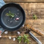 Non-toxic cookware: A cast iron skillet with fresh rosemary, garlic, and pink Himalayan salt on a rustic wooden countertop.