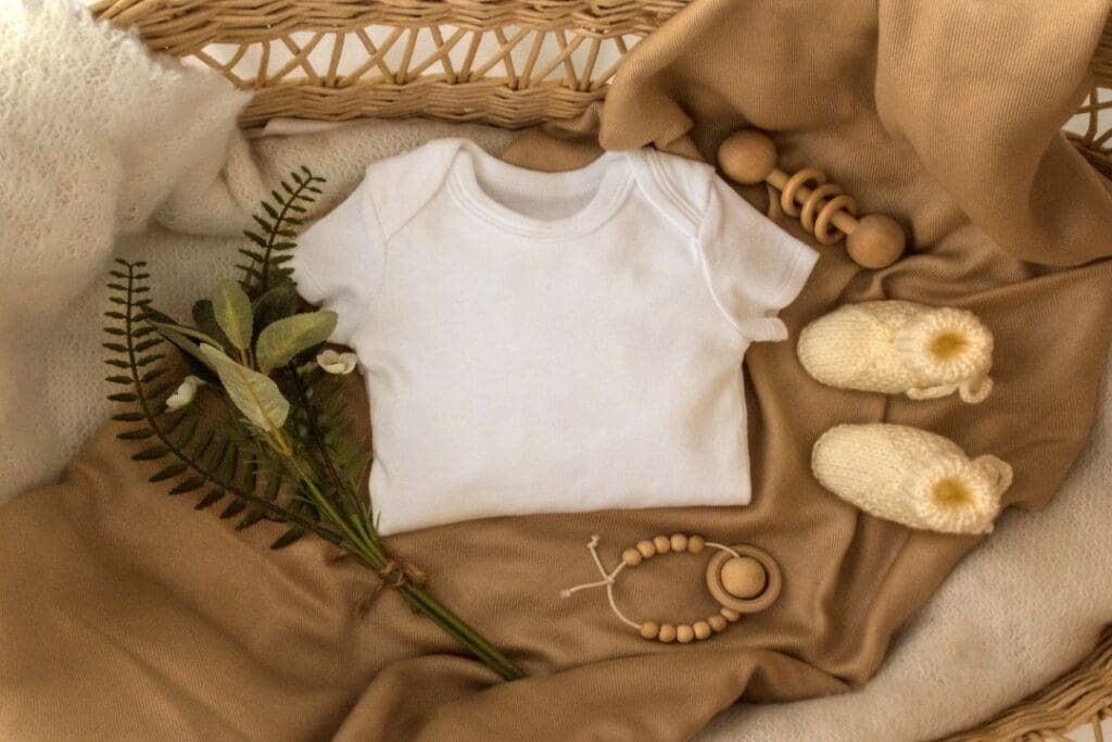 Neutral baby essentials laid out in a cozy basket, featuring a white onesie, knitted booties, a wooden teething toy, and soft natural fabrics.