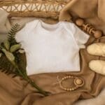 Neutral baby essentials laid out in a cozy basket, featuring a white onesie, knitted booties, a wooden teething toy, and soft natural fabrics.